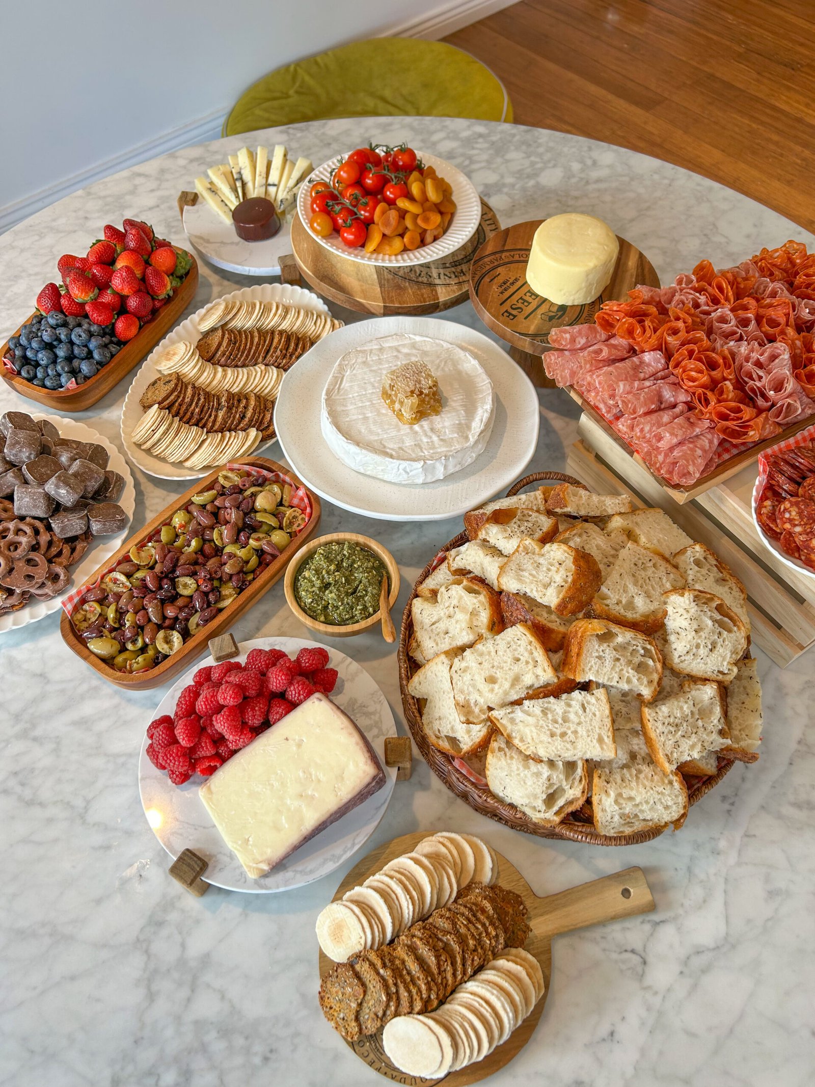 Assorted charcuterie spread with cheeses, cured meats, crackers, bread, berries, olives, and cherry tomatoes on a marble table.